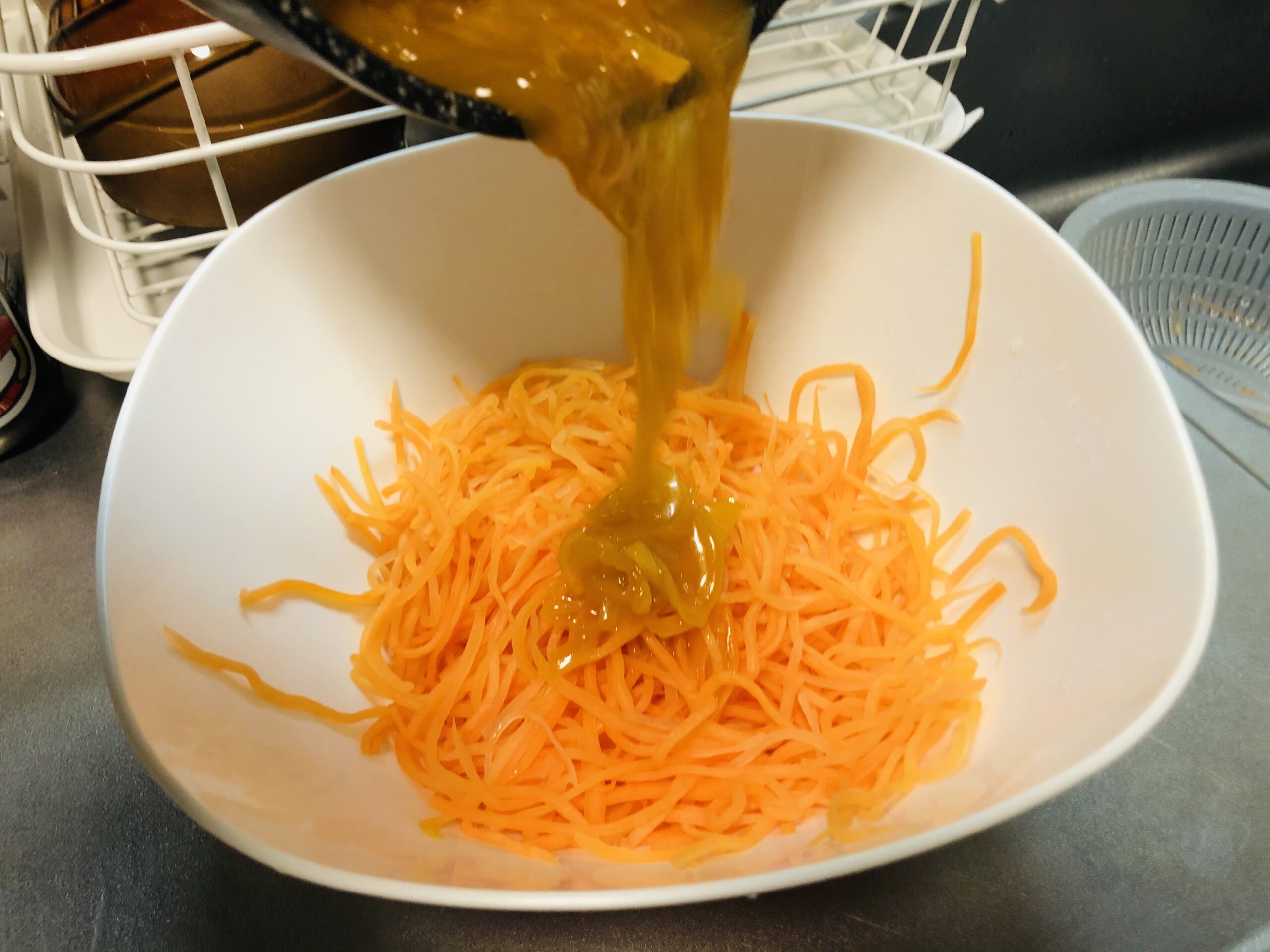 水気を拭き取ったニンジンの細切りに煮詰まった白ワインビネガー入りのオレンジジュースを入れている様子の画像です