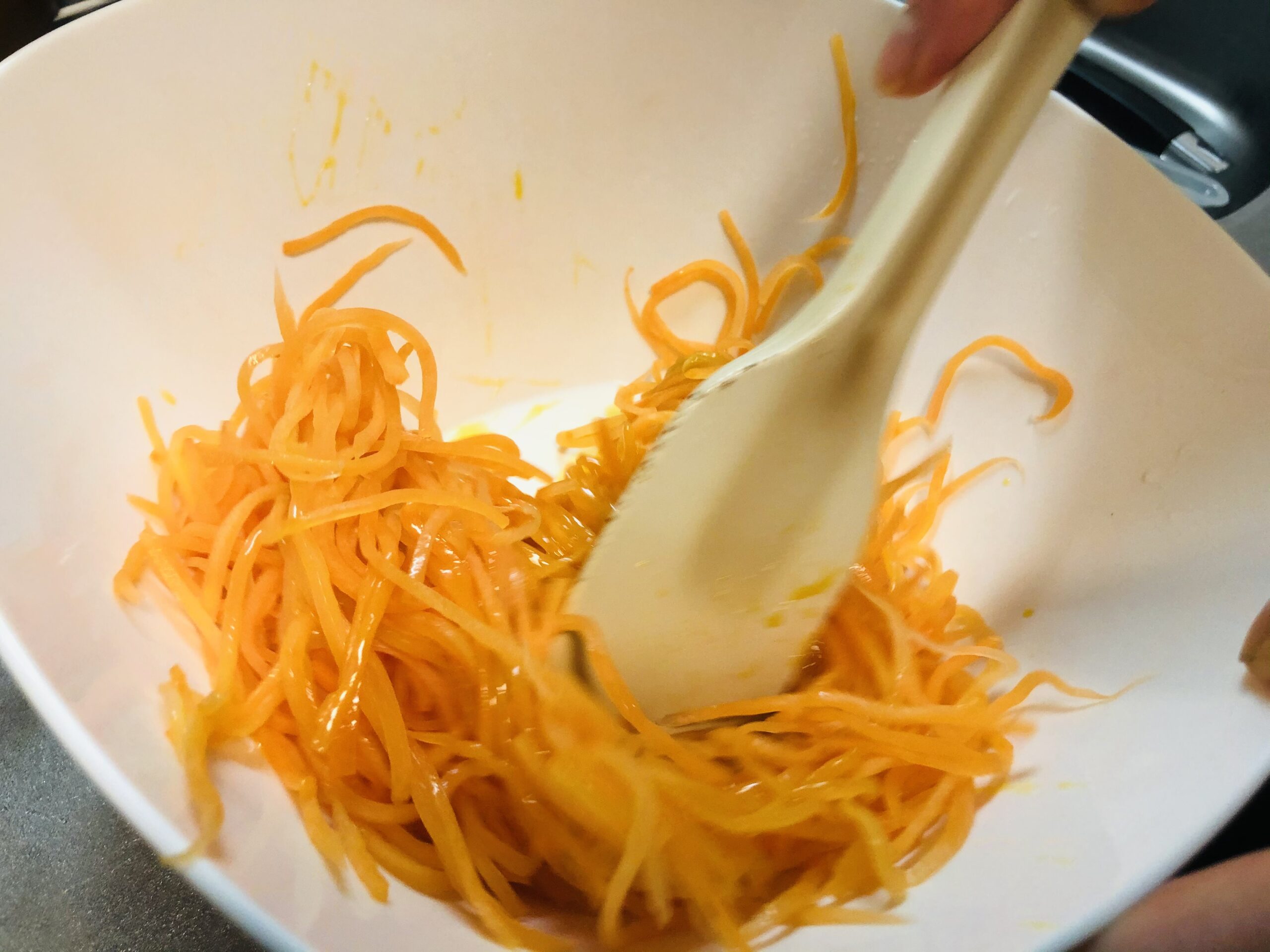 煮詰めたオレンジジュースとニンジンの細切りをゴムベラで混ぜ合わせている様子の画像です