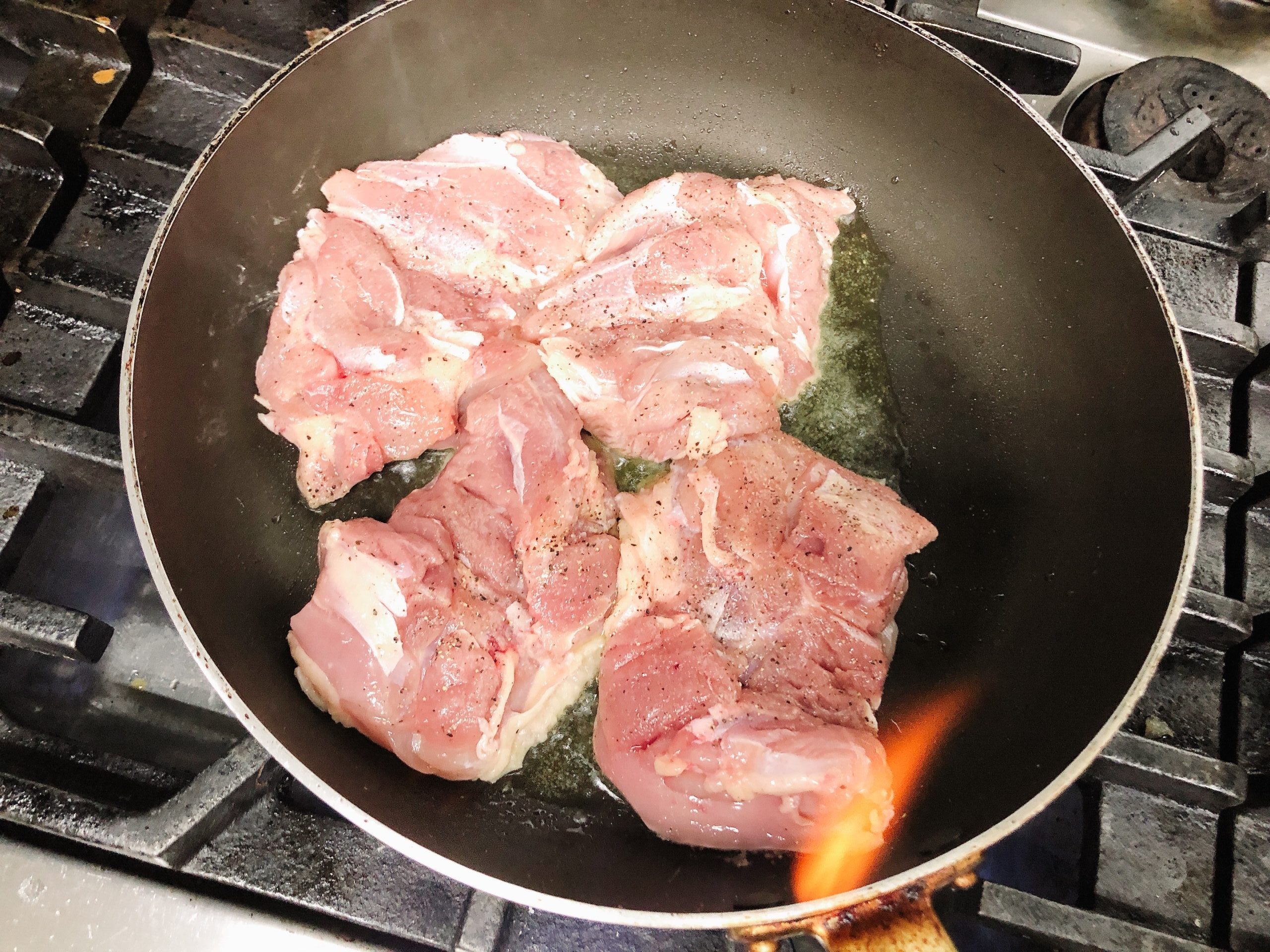 熱したフライパンに油をひいて、皮目から下味をつけた鶏肉を焼いている様子の画像です