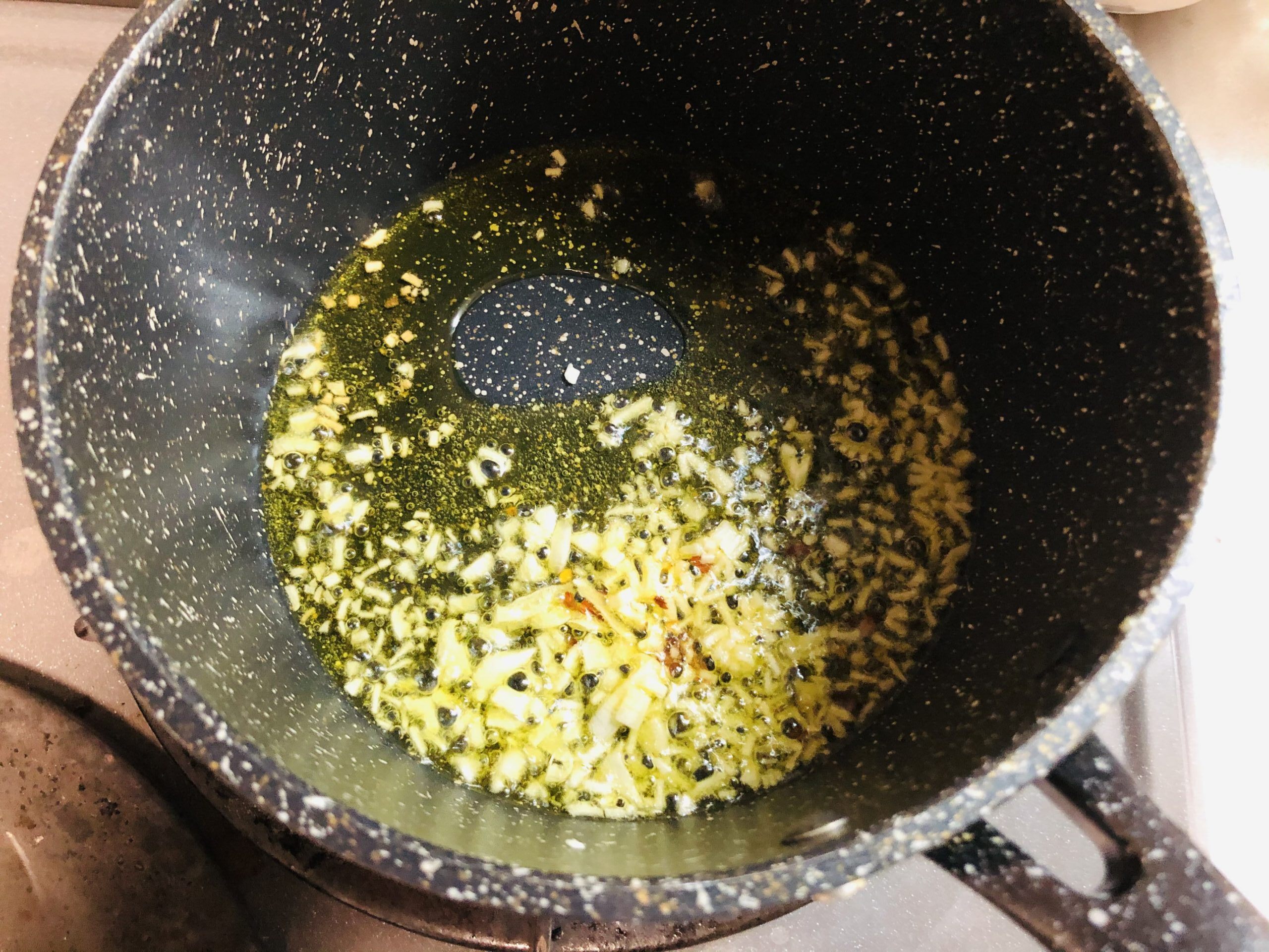 小鍋にオリーブオイルとにんにくみじん切りタカノツメを入れ火にかけて香りを出している様子の画像です
