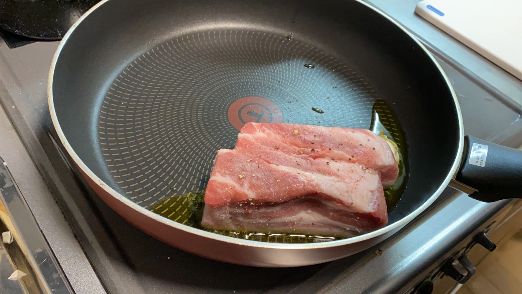 豚バラ肉を皮付きにんにくとオリーブオイルで脂身からフライパンで焼いている様子の画像です