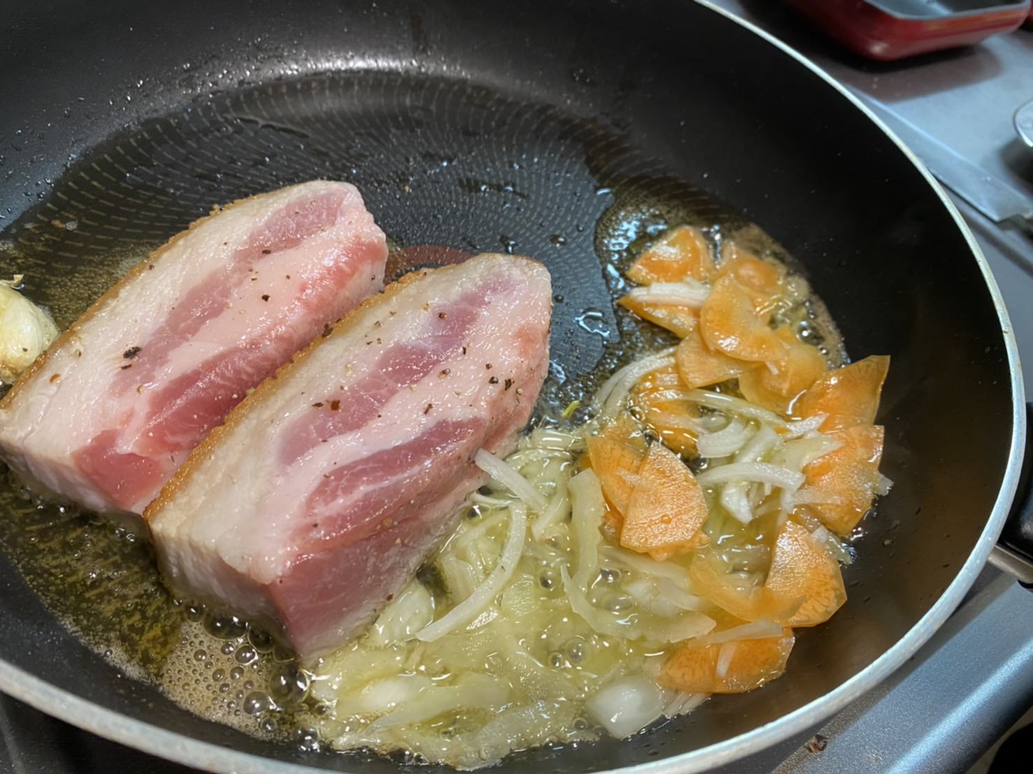 豚バラブロックの２面目を焼き始め、香味野菜の端材を入れて炒めている様子の画像です。