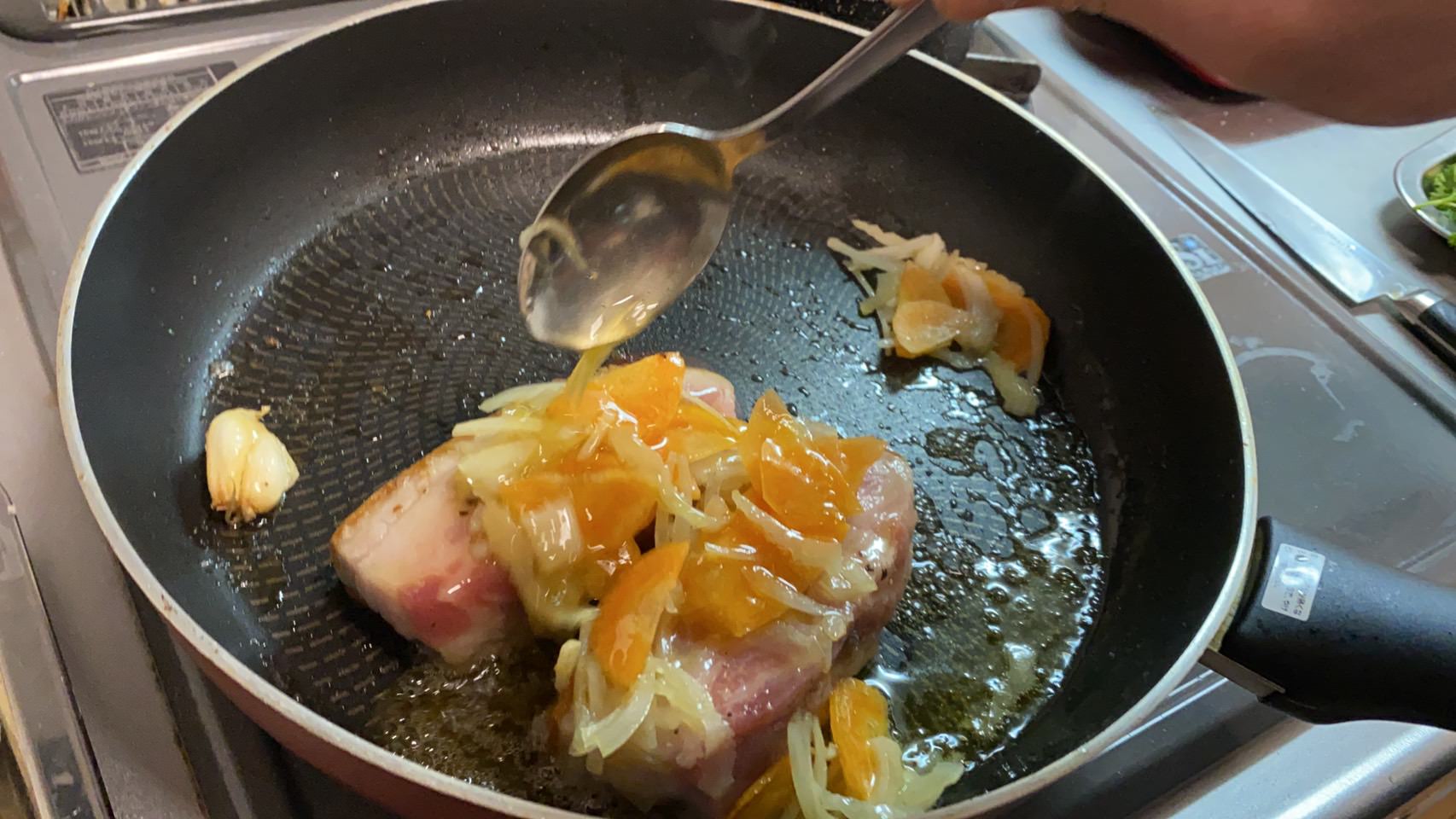 豚バラ肉にしんなりとした香味野菜と焼き油をかけながら焼いている様子です。
