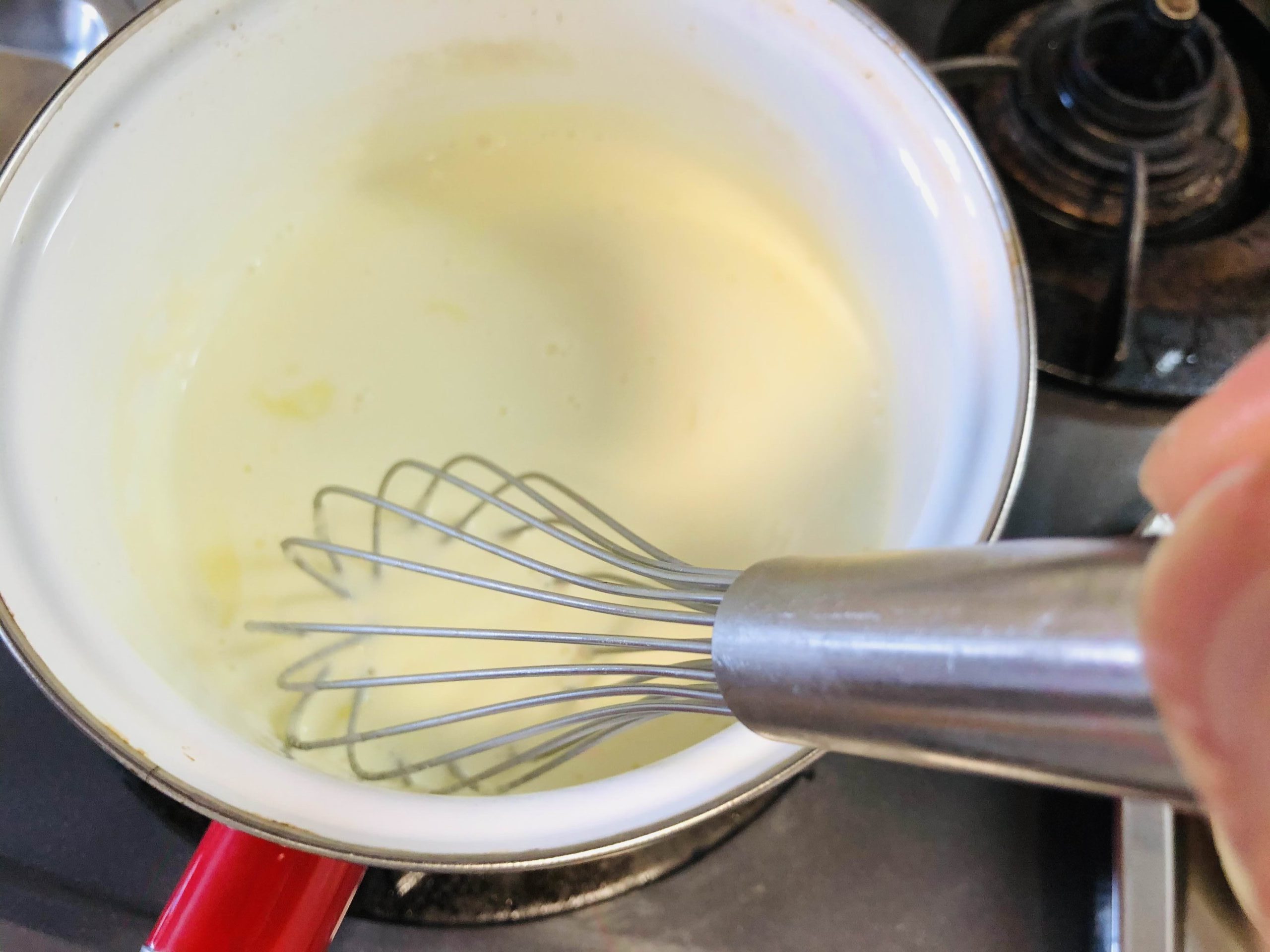 少し柔らかくなったゼラチンの水分を絞りクリームの鍋に入れホイッパーに持ち替えてゼラチンを溶かし混ぜる様子の画像です