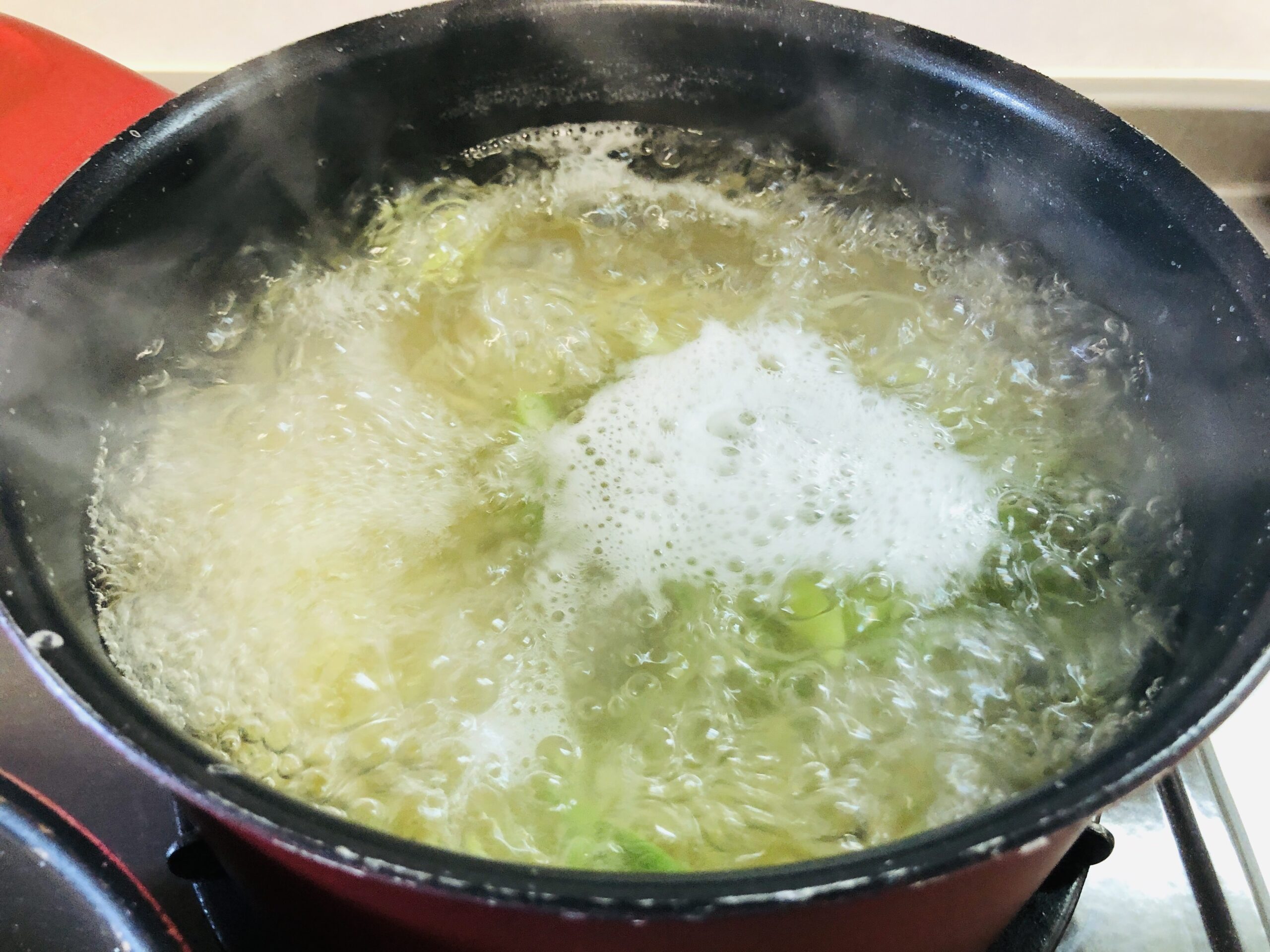 パスタを茹でている鍋にアスパラのスライスを加えた状態の画像です