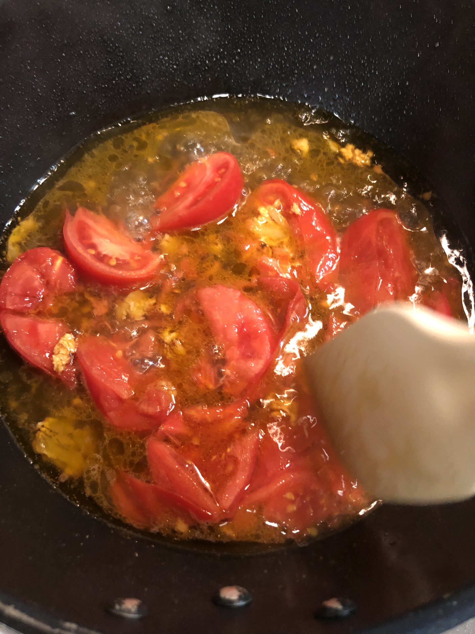 ゴムベラでトマトを潰しながら煮込んでいる様子の画像です