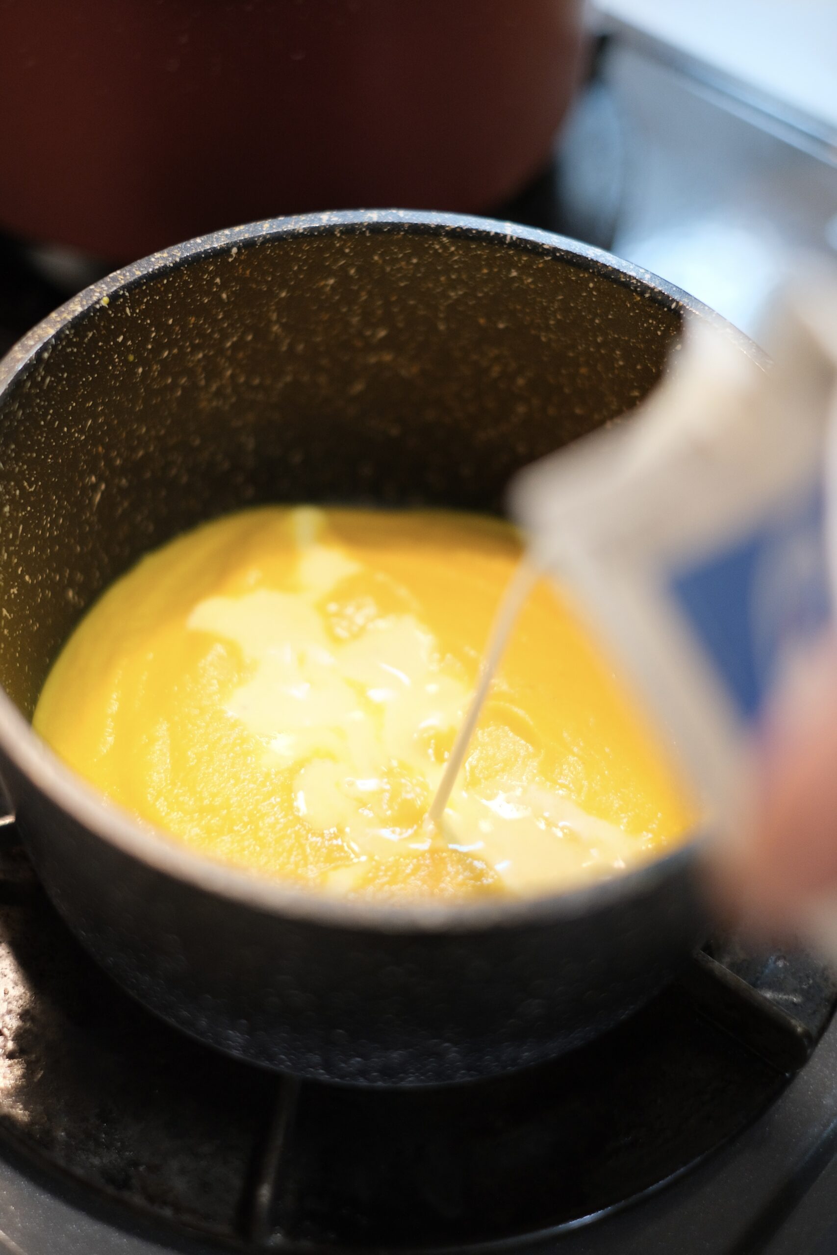 ピュレ状になった人参スープのベースに牛乳を加えているようすの画像です