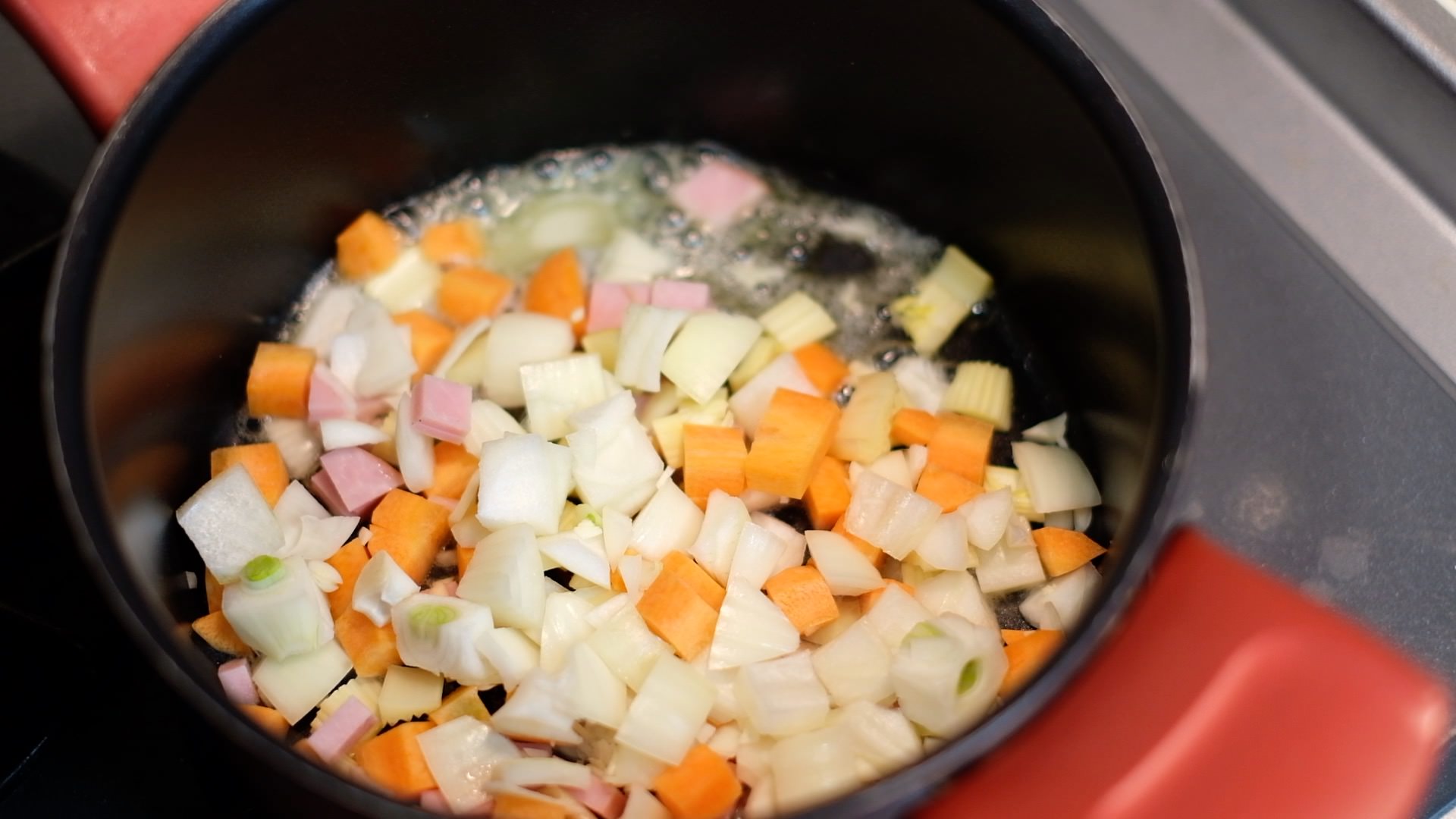 バターを加熱した鍋に香味野菜とハム、塩を少々加え、中火で炒める様子の画像です