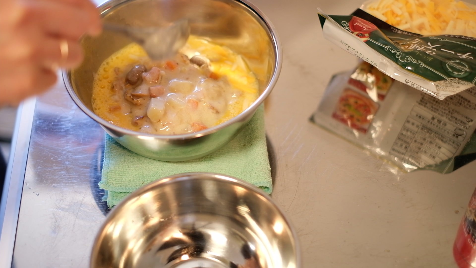 チーズや生クリームを加え温めたクラムチャウダーを溶いた卵のボウルに加える様子の画像です